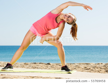 Woman exercising yoga at sea beach 53769458
