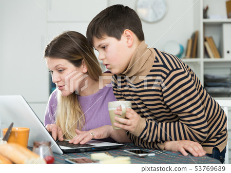 Portrait of young woman and son chatting at table with laptop 53769689