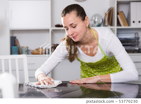 Young woman in an apron cleans the table at home Young woman in an apron cleans the table at home 53770230