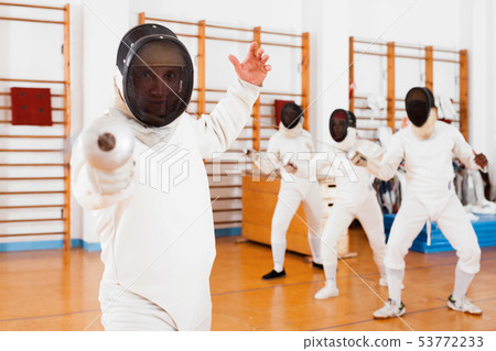 Sporty young man fencer practicing effective fencing techniques in training room Sporty young man fencer practicing effective fencing techniques in training room 53772233