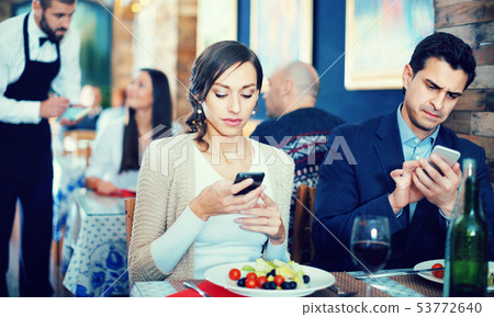 Portrait of man and woman in the restaurant with mobile phones Portrait of man and woman in the restaurant with mobile phones 53772640