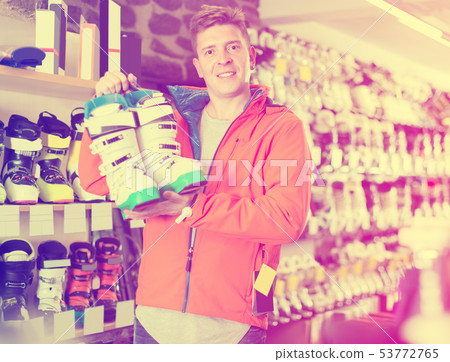 Man 22-28 years old in helmet and jacket is demonstrating ski boots Man 22-28 years old in helmet and jacket is demonstrating ski boots 53772765