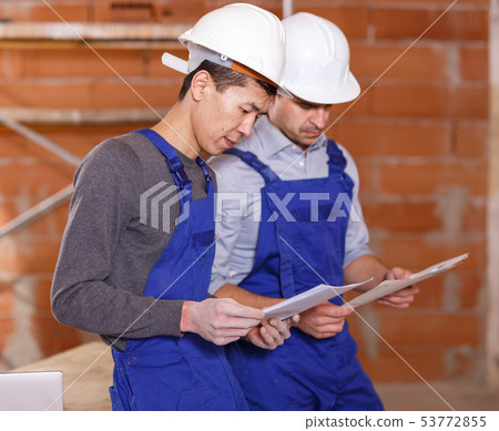Builders reading plan of brick building 53772855