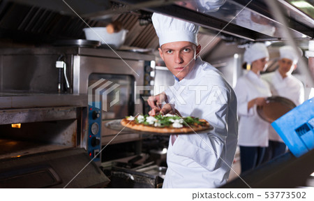 Young chef getting pizza out of oven 53773502