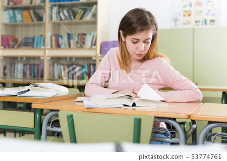 Girl is sitting at the desk and writing homework 53774761