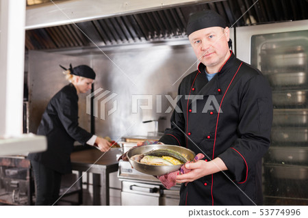 Cook offering to taste baked fish 53774996