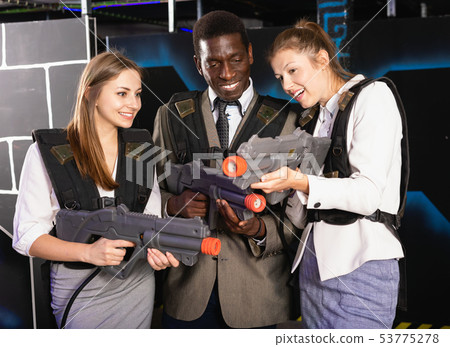 Smiling associates – afro man and two European women posing at laser tag room Smiling associates – afro man and two European women posing at laser tag room 53775278