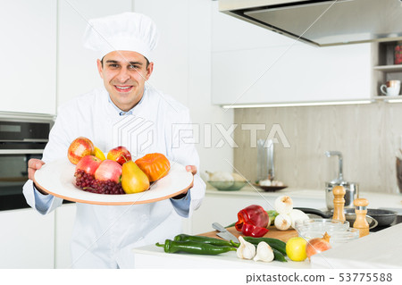 Professional male chef holding big plato with fruits in white uniform 53775588