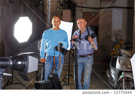 two photographers standing with cameras among professional photo equipment two photographers standing with cameras among professional photo equipment 53775844
