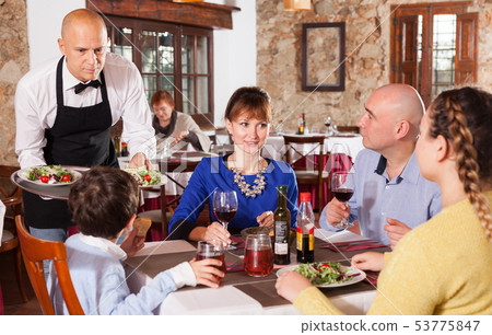 Waiter serving dishes to family Waiter serving dishes to family 53775847