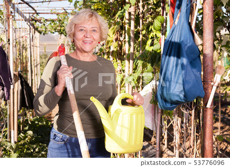 Woman posing with watering can in garden Woman posing with watering can in garden 53776096