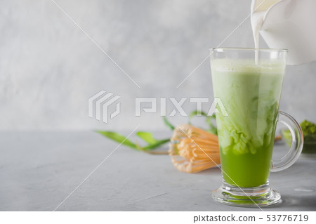 Green matcha tea and milk in latte glass on grey Green matcha tea and milk in latte glass on grey 53776719