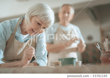 Cropped photo of elderly craftswoman painting decorative plate in workshop 53781195