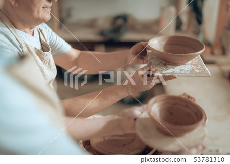 High angle of male craftsman looking at his ceramic bowl in workshop High angle of male craftsman looking at his ceramic bowl in workshop 53781310