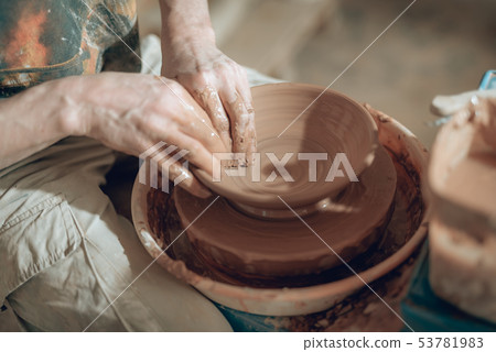 High angle of clay master's dirty arms working on potter's wheel 53781983