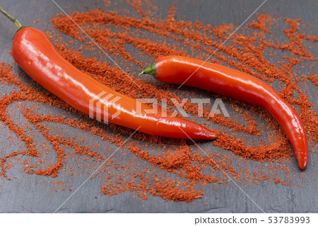 Raw red chili peppers and ground paprika on dark Raw red chili peppers and ground paprika on dark 53783993