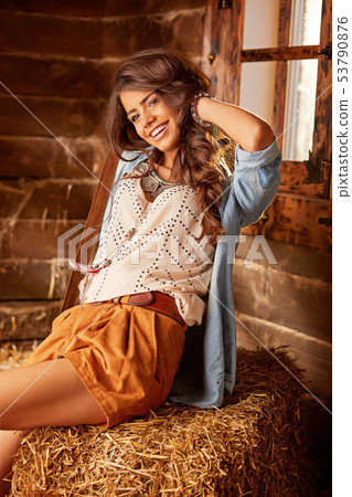 Young girl sitting in barn on bale of hay Young girl sitting in barn on bale of hay 53790876