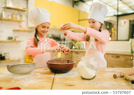 Little sisters cooks in caps kneads eggs in a bow 53797607