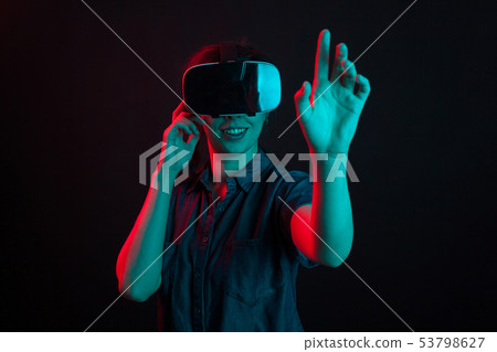 Beautiful young woman smiling with virtual reality helmet in studio and colorful lighting Beautiful young woman smiling with virtual reality helmet in studio and colorful lighting 53798627
