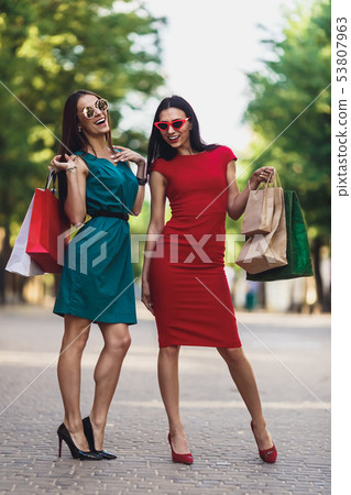 Young attractive girls with shopping bags in the summer city. Beautiful women in sunglasses looking Young attractive girls with shopping bags in the summer city. Beautiful women in sunglasses looking 53807963
