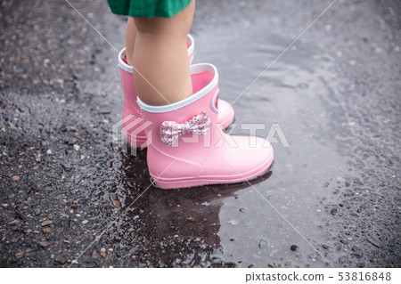 A girl is playing with water wearing rain boots in a puddle 53816848