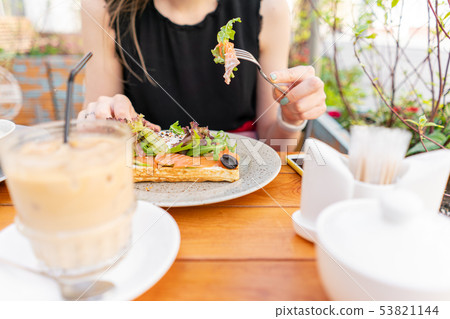 Traditional Belgian waffle with salmon, lettuce leaves and poached egg. A young woman is having 53821144