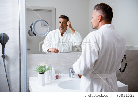 Handsome young man combing his hair in front of the mirror Handsome young man combing his hair in front of the mirror 53831522