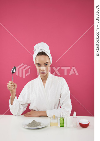 Pretty young lady in bathrobe sitting at the table with cosmetic products Pretty young lady in bathrobe sitting at the table with cosmetic products 53831676
