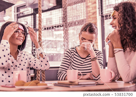 Two women laughing after their friend word explanation while sitting in bakery 53831700