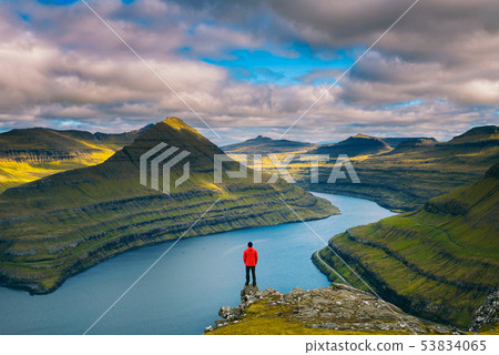 Hiker enjoys views over fjords from a mountain near Funningur on Faroe Islands 53834065