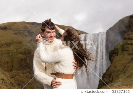 A young smiling couple in warm wedding outfit in front of a waterfall. Closeup  53837365
