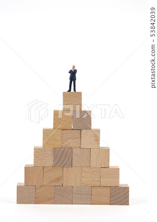 Miniature Businessman Above Wooden Blocks 53842039