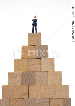 Miniature Businessman Above Wooden Blocks 53842040