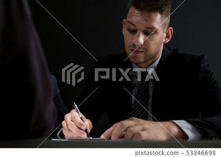 Interrogator takes note while interviewing suspect Interrogator takes note while interviewing suspect 53846698