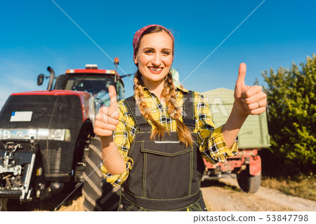 Farmer woman in front of agricultural machinery giving thumbs-up Farmer woman in front of agricultural machinery giving thumbs-up 53847798
