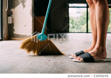 Human legs wearing slippers using sweeping broom inside the house