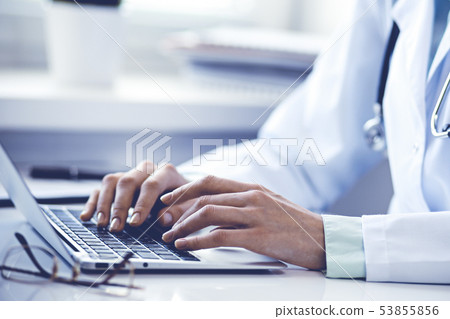 Doctor woman using laptop computer while sitting at the desk near window in hospital. Medicine and 53855856