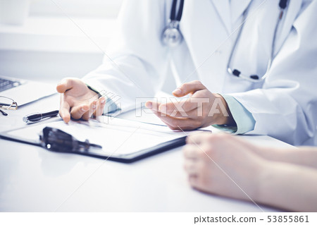 Doctor and female patient sitting at the desk and talking in clinic near window. Medicine and health 53855861