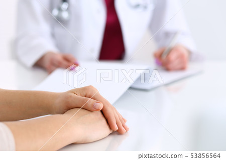 Unknown doctor woman consulting patient while filling up an application form at the desk in hospital 53856564