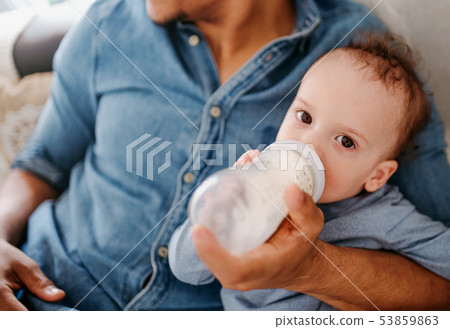 A midsection of father bottle feeding a small toddler son indoors at home. A midsection of father bottle feeding a small toddler son indoors at home. 53859863