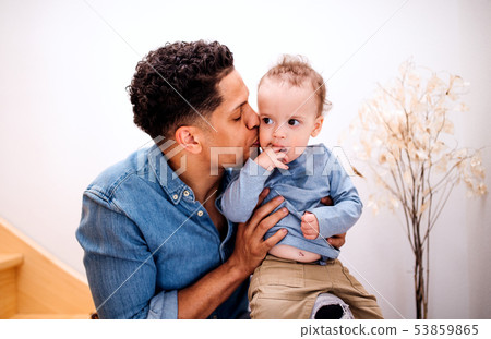 A portrait of father and small toddler son indoors at home, sitting on staircase. A portrait of father and small toddler son indoors at home, sitting on staircase. 53859865