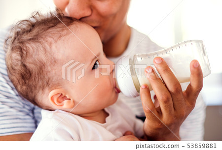 A midsection of father bottle feeding a small toddler son indoors at home. 53859881