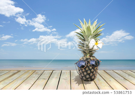 Pineapple with sunglasses and flower on wooden floor next to the beach. Pineapple with sunglasses and flower on wooden floor next to the beach. 53861753