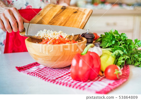 Female hand put chopped garlic in wooden bowl with salad in kitchen. Cooking vegetables Female hand put chopped garlic in wooden bowl with salad in kitchen. Cooking vegetables 53864809
