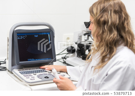 Pretty female doctor, posing while is doing a sonography. Female doctor wearing white coat, holding 53870713