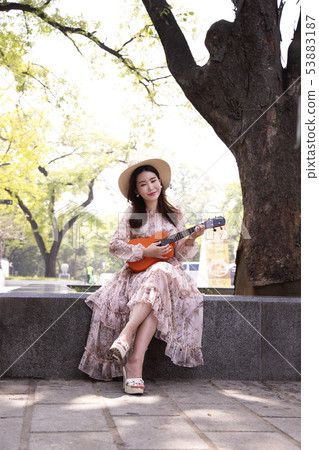 A woman wearing a hat hitting an ukulele 53883187