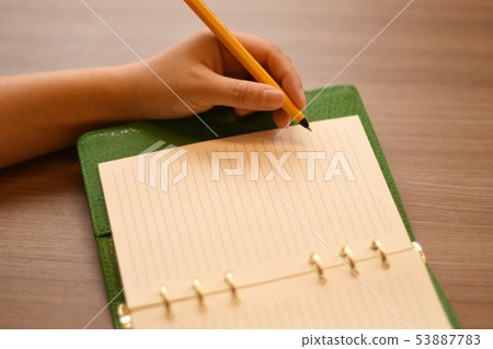 An orange ballpoint pen to write on a green cover system notebook. 2 53887783