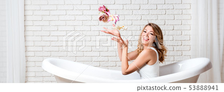 Woman in bath having fun with flowers. Beautiful young blonde woman enjoying pleasant bath, looking Woman in bath having fun with flowers. Beautiful young blonde woman enjoying pleasant bath, looking 53888941