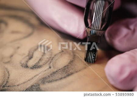Close-up of a tattoo needle. The process of the tattoo master. Pink women's protective gloves. 53893980