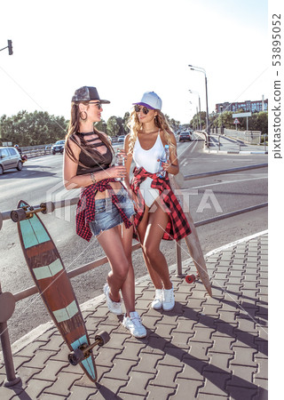 Two girls girlfriends holding water bottles, background road skateboard cars, beautiful tanned Two girls girlfriends holding water bottles, background road skateboard cars, beautiful tanned 53895052